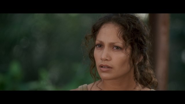 Close-up of a woman with curly hair and a serious expression, set against a blurred green background.