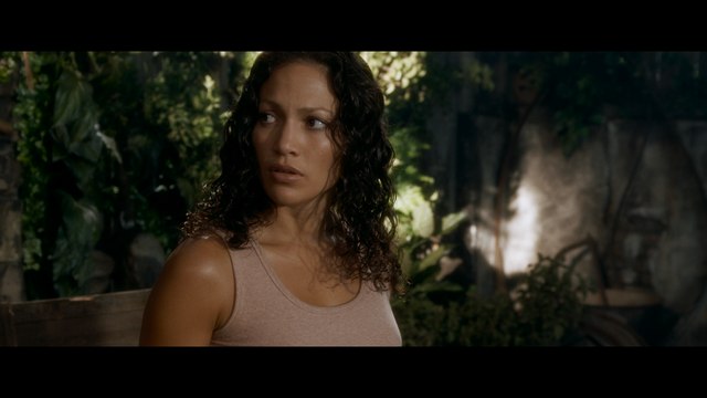 A close-up image of a woman with curly hair, wearing a light tank top, looking concerned in a lush, green environment with blurred plants in the background.