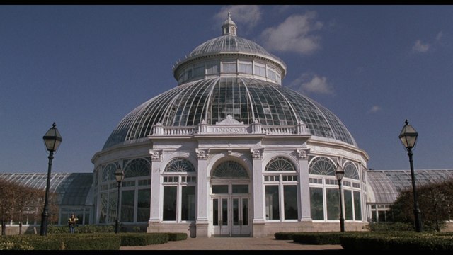 A large glass greenhouse with a domed roof, surrounded by well-maintained greenery and a clear blue sky.