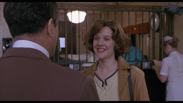 Scene from a movie depicting a woman smiling while talking to a man in a vintage hospital setting.