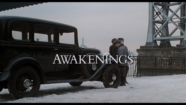 Scene from the movie 'Awakenings' featuring a vintage black car parked on a snowy street with characters standing nearby.