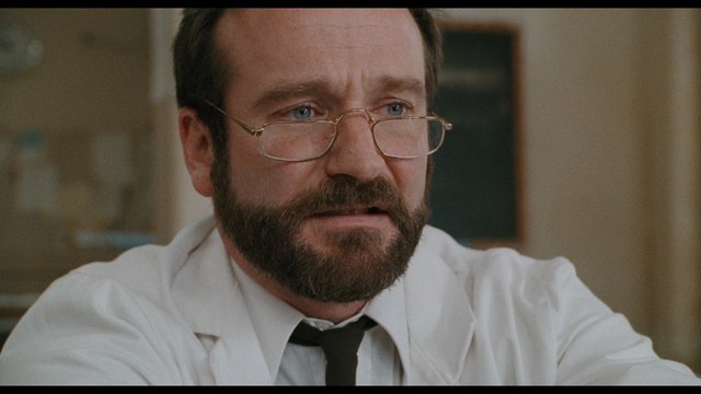 Close-up of a man with a beard and glasses, wearing a white lab coat, displaying an intense expression, likely in a medical or therapeutic setting.