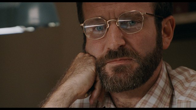 Close-up of a man with glasses and a beard, looking contemplative while resting his chin on his hand.