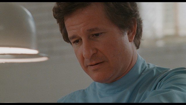 A man in a blue medical scrubs looking down thoughtfully while engaged in a task.