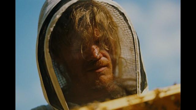 Statue of a smiling figure resembling Jesus, giving a thumbs up gesture, set against a colorful backdrop with signs related to Catholicism.