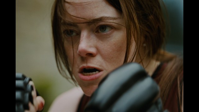 A scene from a movie featuring two young men sitting closely together in an airport waiting area, with one holding a box of popcorn.