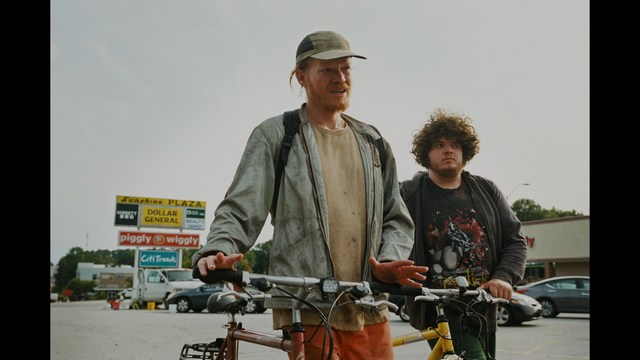 A group of people standing in a church, with a focus on a woman in a striped blazer looking up, while others are holding books or looking ahead.