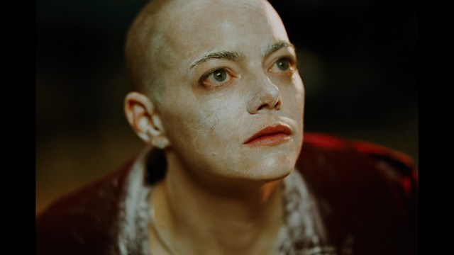 A woman with dark hair and a neutral expression sitting in a retro diner setting.