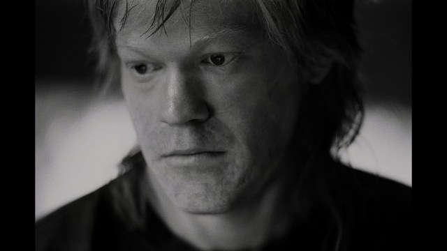 A young man pointing a handgun while seated in a bus, showcasing an intense expression.