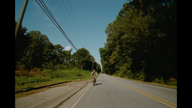 A worried woman stands on a deserted road, looking shocked or distressed as she gazes into the distance.