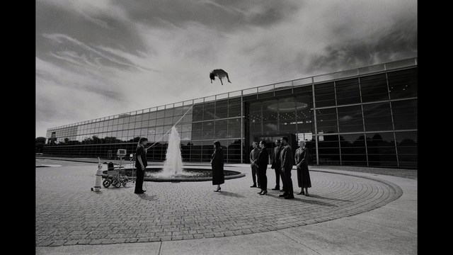 Close-up of a woman with long black hair sitting in a restaurant, looking concerned. A colorful painting is visible in the background, along with red bar stools.