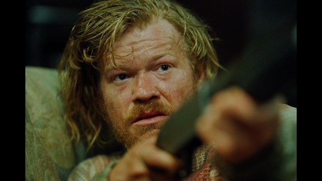 A close-up shot of a man wearing a white suit and a white hat, looking intently at someone in a retail store filled with merchandise.
