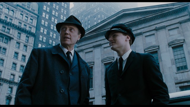 Statue of a smiling figure resembling Jesus, giving a thumbs up gesture, set against a colorful backdrop with signs related to Catholicism.