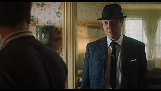 A scene from a movie featuring two young men sitting closely together in an airport waiting area, with one holding a box of popcorn.