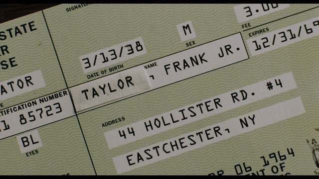 A close-up of a man with a concerned expression, with blurred figures in the background, set in a dimly lit interior.