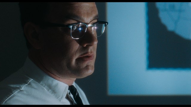 A scene featuring a man with short hair and a beard, wearing a brown jacket and purple shirt, standing outside a restaurant with bright yellow walls and a cartoon cow logo.