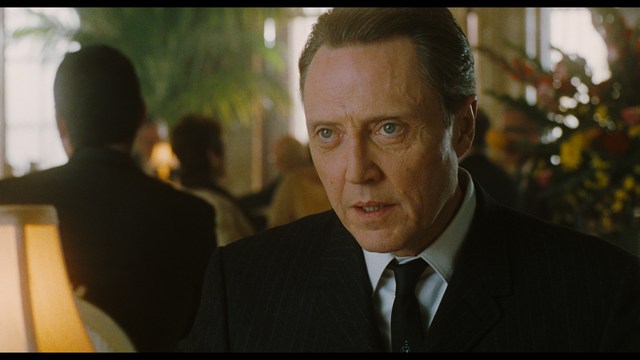 Two men are engaged in conversation at a colorful playground with bright slides in the background.