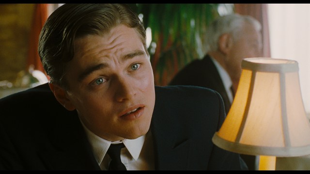 A scene featuring five characters in a bar setting, with a focus on their expressions and interactions. The backdrop includes bar shelves with bottles and a bartender visible in the background.