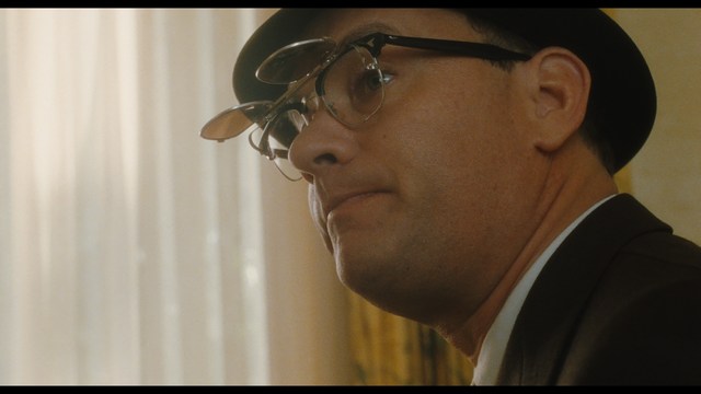 A man with short hair and a beard sits at a table, looking surprised or excited while holding a bottle.