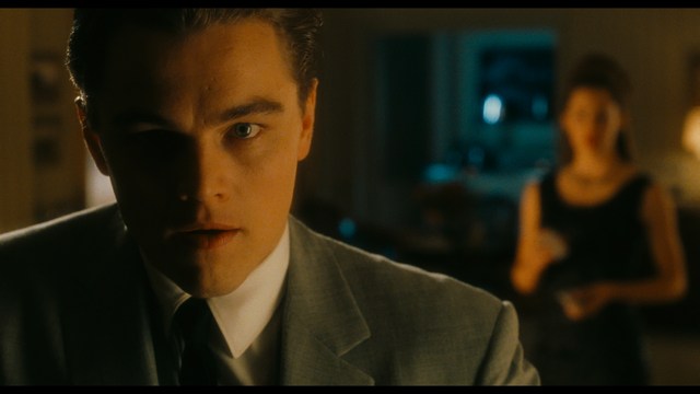 Two young men are looking at something off-camera, standing inside a building with bright lighting and seating areas visible in the background.