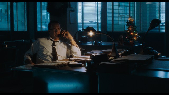 A close-up shot of a man wearing a white suit and a white hat, looking intently at someone in a retail store filled with merchandise.