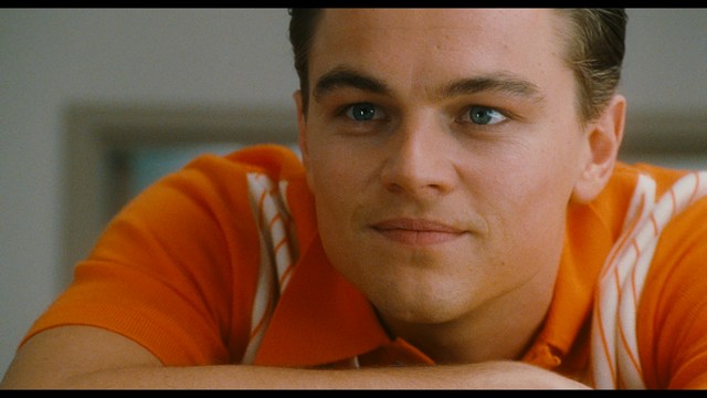 A man with dark, styled hair and a subtle smile seated at a restaurant table, with blurred diners in the background.