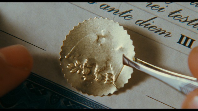 A serious-looking cardinal with a red hat and black robes sitting in a wooden chair in an office, surrounded by colorful posters and memorabilia.