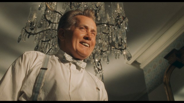 A tense scene featuring a woman with long hair and a serious expression, looking off to the side, while a man with short hair sits in the background, appearing relaxed and slightly turned away.