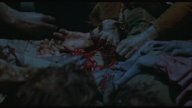 A close-up of several hands gripping and interacting with a gory, bloodied scene, depicting a violent or traumatic moment.
