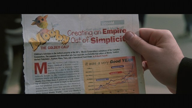 A person holding a newspaper article titled 'Mooby: Creating an Empire Out of Simplicity' featuring a chart showing growth, alongside an image of a cartoon cow.
