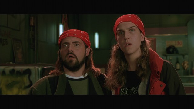 Scene from the movie featuring two characters, one with a beard and the other with long hair, both wearing red bandanas and looking surprised.