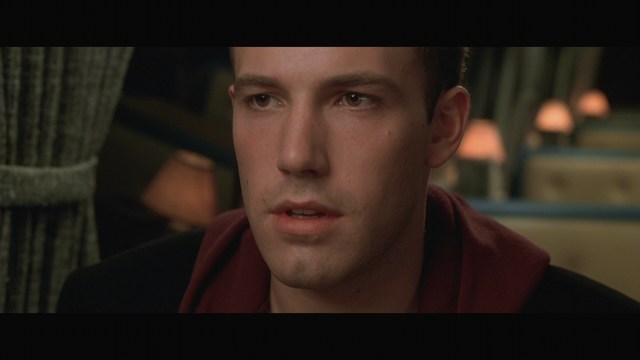 A man wearing a white suit and hat appears to be having a serious conversation in a retail store, with various products displayed in the background.