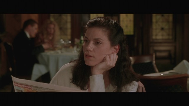 A woman sitting at a restaurant table, resting her chin on her hand while reading a newspaper.