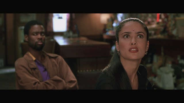 A scene featuring a man sitting with his arms crossed, looking away, and a woman with a concerned expression, seen in a dimly lit bar setting.