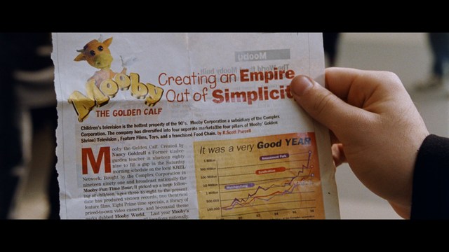 A close-up of a person's hand holding a crumpled newspaper with the headline "Mooby's: Creating an Empire Out of Simplicity" and a graphical chart showcasing growth, titled "It was a very Good YEAR."
