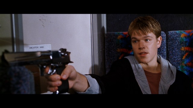 A young man pointing a handgun while seated in a bus, showcasing an intense expression.