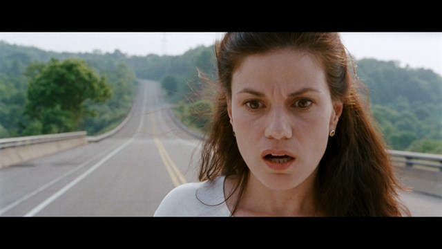A worried woman stands on a deserted road, looking shocked or distressed as she gazes into the distance.
