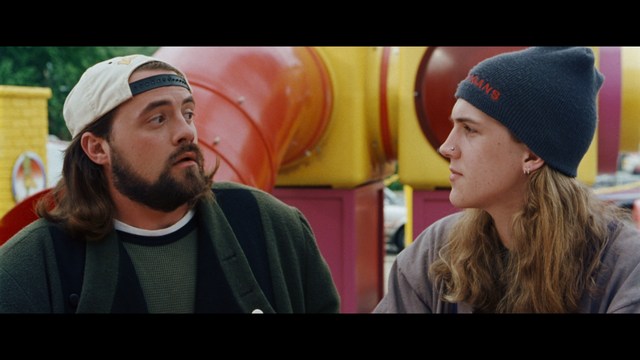 Two men are engaged in conversation at a colorful playground with bright slides in the background.