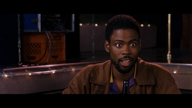 A man with short hair and a beard sits at a table, looking surprised or excited while holding a bottle.