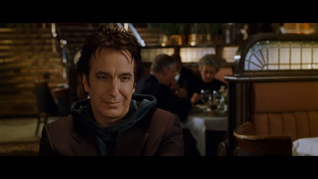 A man with dark, styled hair and a subtle smile seated at a restaurant table, with blurred diners in the background.