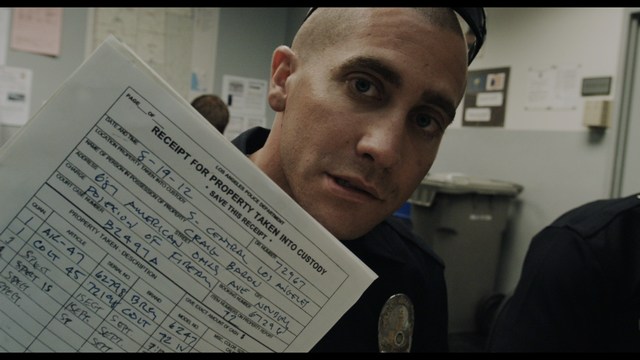 Two young men are looking at something off-camera, standing inside a building with bright lighting and seating areas visible in the background.