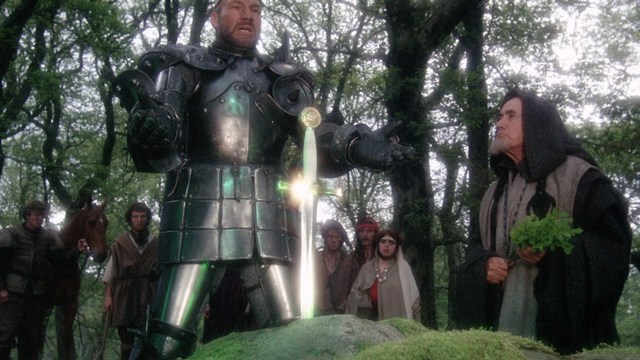Scene featuring three characters on a roadside, discussing animatedly. A green landscape is visible in the background.