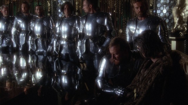 Close-up of a man with a serious expression, featuring details of his face and suit against a softly lit background.