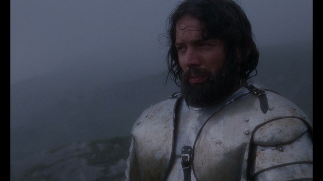 A close-up of an elderly man with a beard and white attire, appearing serious and contemplative, set against a colorful, futuristic background.