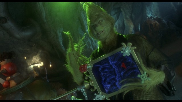 A woman with long dark hair resting her chin on her hand, looking pensively off to the side. In the background, various kitchen appliances and items are visible.