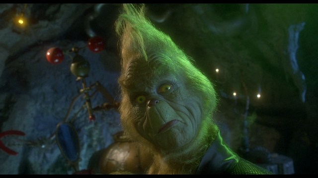 A man in a white suit and hat stands at the entrance of a house, smiling, with a suburban neighborhood visible in the background.