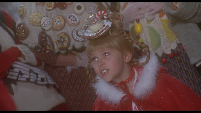 Two men sitting close together in a diner, one wearing a black beanie with the word 'SNOOGANS' and the other wearing a cap, both appearing engaged in conversation.