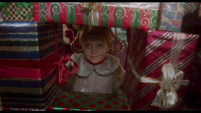 A still from a movie featuring a man standing on a boardwalk in front of an arcade with signs for Skeeball, saltwater taffy, and various attractions.