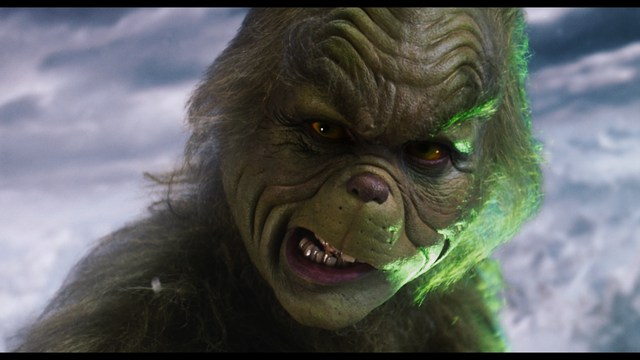 A serious-looking cardinal stands in front of a wooden backdrop with colorful posters related to Catholicism, holding a microphone at a press conference.