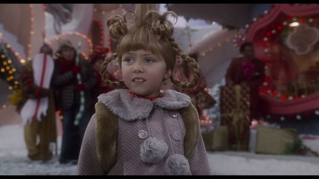 Statue of a smiling figure resembling Jesus, giving a thumbs up gesture, set against a colorful backdrop with signs related to Catholicism.